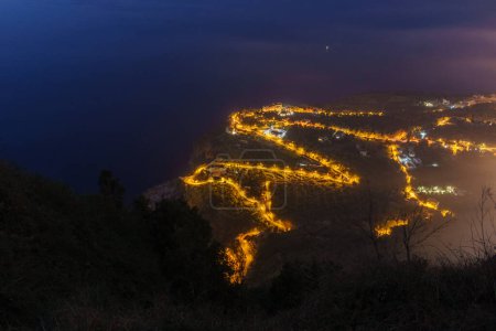 Luftaufnahme der beleuchteten Serpentinenstraße am Mittelmeer von der Abenddämmerung in der Nacht, Palmi, Kalabrien, Italien