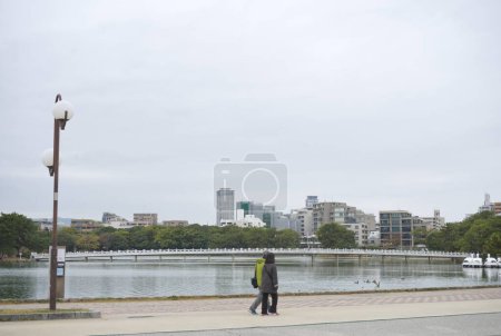 Photo for Fukuoka, Japan - December 4, 2022: Riverside atmosphere of Ohori Park, bridge and city in the background - Royalty Free Image