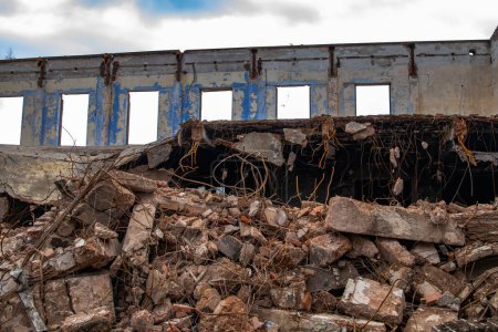 Abriss eines Industriegebäudes. Im Vordergrund sind die Überreste von gebrochenem Stahlbeton zu sehen. Im Hintergrund stehende Außenwand mit Fenstern.