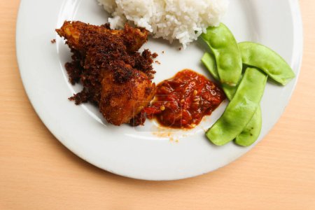 Photo for Rice with Ayam Goreng Lengkuas or Galangal Fried Chicken or Ayam Serundeng with chili sauce or sambal cobek and kacang roay (Phaseolus lunatus) as a vegetable. Indonesian dish concept - Royalty Free Image