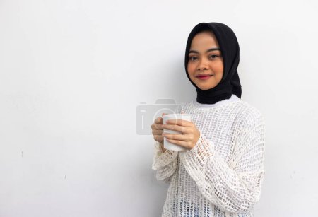 Photo for Beautiful smiling hijab woman in casual white shirt holding the mug isolated over gray background. - Royalty Free Image