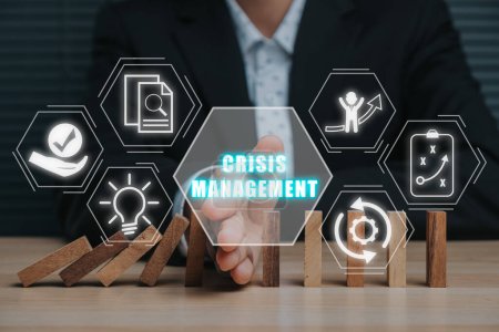 Krisenmanagement-Konzept, Geschäftsmann stoppt fallende Dominosteine mit der Hand auf dem Schreibtisch mit Krisenmanagement-Symbol auf virtuellem Bildschirm.
