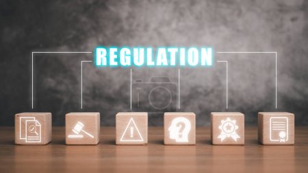 Concept de régulation, bloc en bois sur bureau avec icône de régulation sur écran virtuel, marteau, ordinateur portable et livre juridique sur table en bois blanc.