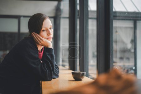 Photo for Sad woman sitting by the window looking outside - Royalty Free Image