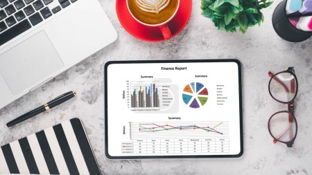Concepto de análisis de negocios, una tableta que muestra un informe financiero con gráficos coloridos junto a una taza de café rojo, computadora portátil y artículos de papelería sobre un fondo de mármol