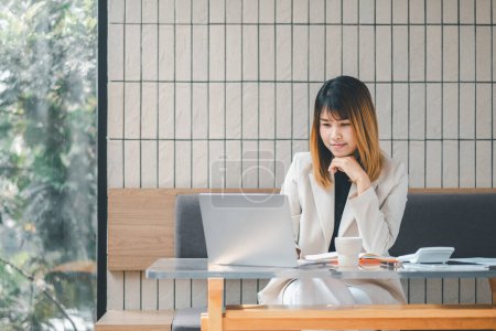 Eine nachdenkliche Geschäftsfrau in tiefen Gedanken, während sie an ihrem Laptop in einem gut beleuchteten Café arbeitet, umgeben von ihren Arbeitsmaterialien