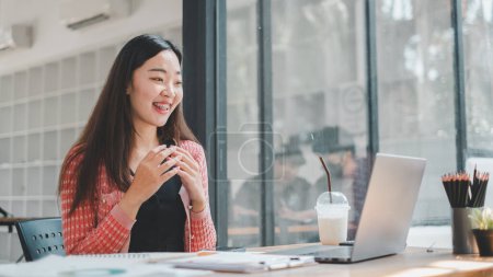 Photo for Business analytics concept, A happy young woman with braces is seen enjoying her work on a laptop at a cafe desk, with a refreshing iced drink by her side - Royalty Free Image