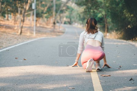 Photo for Fitness concept, A woman in fitness attire crouches at the starting position on a park path, preparing for a morning run - Royalty Free Image