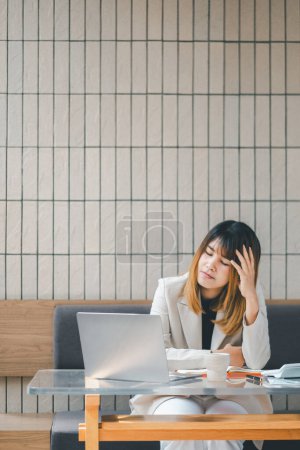 Stressed businesswoman at a cafe with laptop, showing signs of fatigue or headache during a busy workday