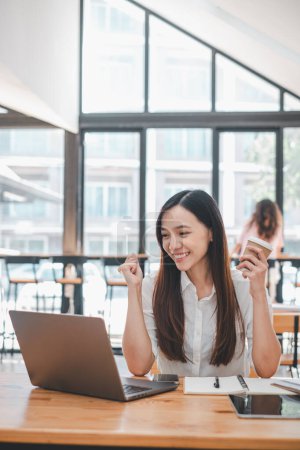 Business Analytics-Konzept: Fröhliche Asiatin kauft online mit Kreditkarte ein und feiert eine erfolgreiche Transaktion auf ihrem Laptop in einem Café