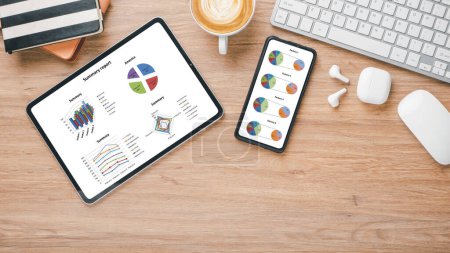 Arbeitsplatz mit Tablet und Smartphone mit bunten Tortendiagrammen und Diagrammen für Business Analytics, begleitet von einer Tasse Kaffee