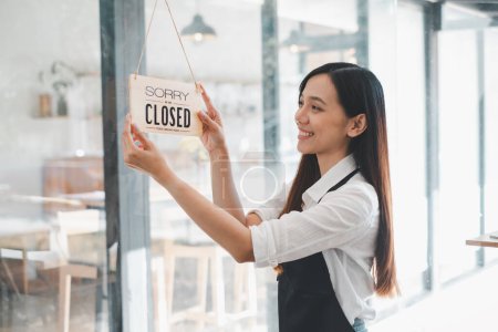 Une propriétaire de café affiche un panneau "Désolé, nous sommes fermés" avec un sourire de contenu, marquant la fin d'une journée de travail enrichissante dans son établissement accueillant.