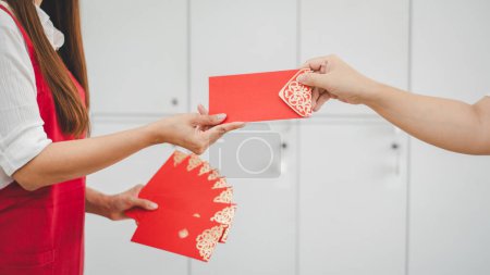 Hände von zwei Personen tauschen einen roten Umschlag mit aufwändigen Goldmustern aus, ein Brauch, der in asiatischen Traditionen gute Wünsche und Glück symbolisiert..