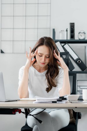 Frau sitzt an ihrem Schreibtisch im Büro und massiert ihre Schläfen in einem Moment von Stress und Erschöpfung inmitten eines anstrengenden Arbeitstages.