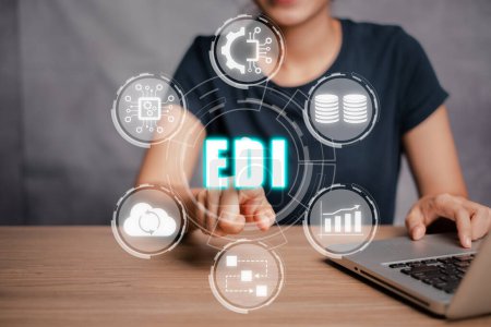 EDI, Electronic data interchange concept, Businesswoman using laptop computer on desk and hand touching electronic data interchange icon on virtual screen.