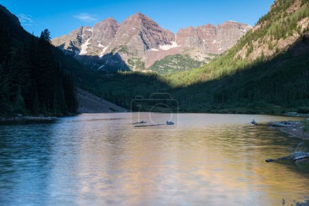 Rising sunlight on the Maroon Bells in Mid-Summer with Maroon Lake in the foreground. The Maroon Bells are located in Central Colorado near the town of Aspen.