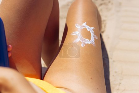 Téléchargez les photos : Belles jambes femelles bronzées sur la plage, gros plan, le soleil est dessiné sur la jambe avec de la crème solaire blanche. Photo de haute qualité - en image libre de droit