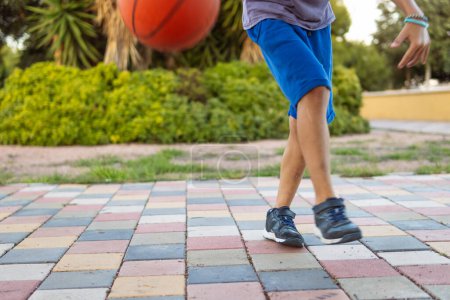 Un garçon joue au basket-ball dans le parc, gros plan sur ses pieds et la balle, capturant l'essence des sports de plein air et de l'énergie de la jeunesse.