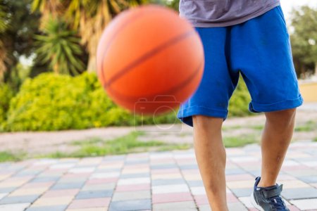 Un garçon joue au basket-ball dans le parc, gros plan sur ses pieds et la balle, capturant l'essence des sports de plein air et de l'énergie de la jeunesse.