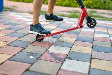Eine Nahaufnahme im Park konzentriert sich auf die Füße eines Jungen und seinen Roller und fängt die Essenz von Spielen im Freien und jugendlicher Freude ein 