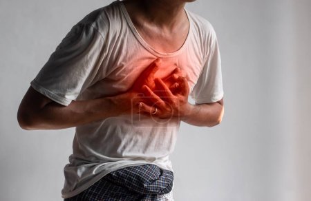 Photo for Asian young man suffering from central chest pain. Chest pain can be caused by heart attack, myocardial infarct or ischemia, myocarditis, pneumonia, stress, etc. - Royalty Free Image