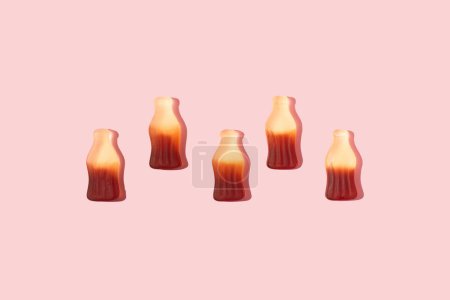 Bottle shaped gummy candies with sunlight shadows assorted in a line on pink background.sugar