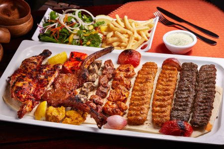 Téléchargez les photos : Barbecue épicé Plat de grillades mixtes avec tikka boti kababs, frites, salade et raita servi dans un plat isolé sur la table vue latérale de la nourriture du Moyen-Orient - en image libre de droit