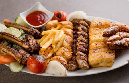 persian mix grill platter with tikka boti, lamb chop, meat kabab, fish, fries and tomato sauce served in dish isolated on grey background top view of arabic food