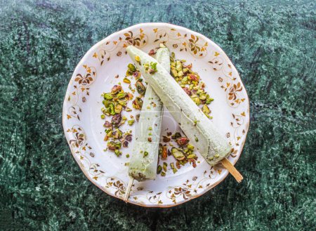 Téléchargez les photos : Shahi kulfi ou kulfi comprennent khoya, lait, pista, pistache avec bâton servi dans un plat isolé sur fond vue du dessus de la crème glacée pakistanaise et indienne - en image libre de droit