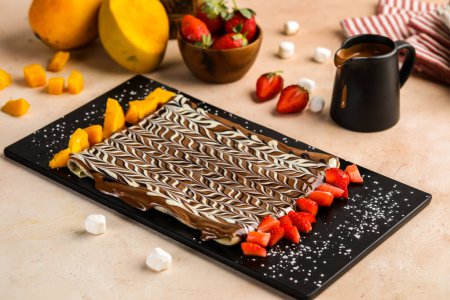 Nutella chocolate crepe garnished with strawberry and mango slice served in dish isolated on table top view of cafe dessert