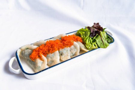 Photo for Fish skin Steamed dumplings with grapefruit sauce and spinach leaves served in tray isolated on background side view of japanese seafood on table - Royalty Free Image