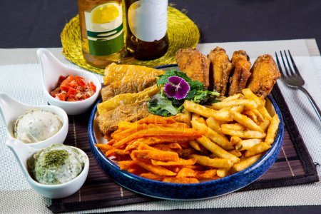 Photo for Snack platter include potato chips, french fries, fried mushroom, chicken wings and fish fry served in dish isolated on napkin side view of unhealthy food on table - Royalty Free Image