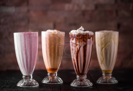 Téléchargez les photos : Agitations assorties de banane, fraise, crème et chocolat servies dans un verre isolé sur une table en bois vue de côté de la boisson arabique - en image libre de droit