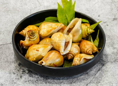 Téléchargez les photos : Escargot cuit à la vapeur avec de la citronnelle ou oc nhay hap xa, bo toi, muoi tac stir fried gonggo servi dans un plat isolé sur fond gris vue de dessus de fruits de mer singapore - en image libre de droit