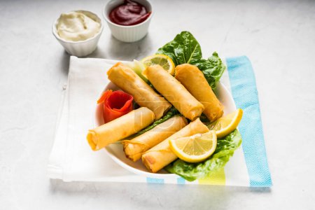 Deep fried Spring Roll with lemon slice and dip sauce served in dish isolated on table top view of arabic food