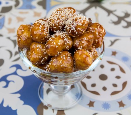 Téléchargez les photos : Boules sucrées Luqaimat ou Gemat aux graines de sésame servies dans un plat isolé sur la table avec vue sur les desserts arabes - en image libre de droit