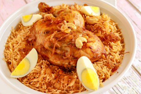 Saudi Chicken Kabsa pulao rice with fried onion, cashew nut and boiled egg served in pot dish isolated on wooden table top view arabic spicy food