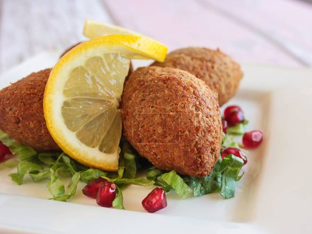 Photo for KEBBAH, kibbeh, kibbe or kubbeh with lemon slice and pomegranate seeds closeup served in dish isolated on table side view of arabic fastfood - Royalty Free Image