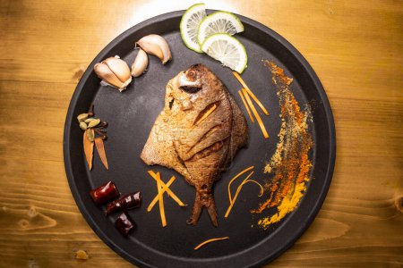 Fried Pomfret Fish or Rupchanda Fry with lime slice served in dish isolated on wooden background top view indian spices, bangladeshi and pakistani food