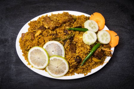 Rindfleisch Yakhni biryani Reispulao mit Gurken, Limettenscheiben und Karotten serviert in Schale isoliert auf dunklem Hintergrund Draufsicht indische Gewürze, bangladeshi und pakistanisches Essen