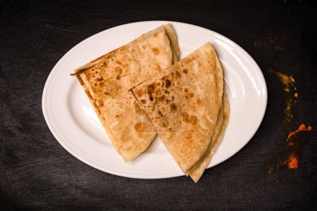 Foto de Paratha Rebanadas servidas en plato aislado sobre fondo oscuro vista superior especias indias, bangladeshi y comida pakistaní - Imagen libre de derechos