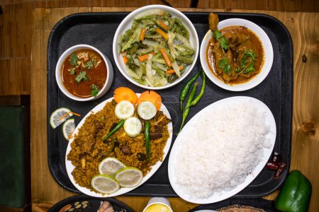 Assorted indian food yakhni biryani, plain rice, chicken rezala, stir fry Mix Vegetables with carrot, capsicum and radish served in dish isolated on wooden background top view of bangladeshi food