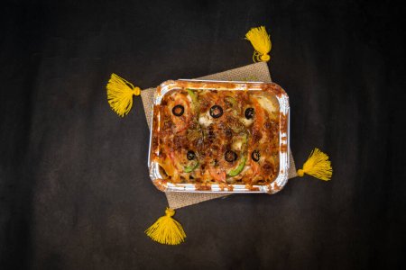 Oven Baked Pasta topping with olive, tomato, capsicum and cheese served in dish isolated on napkin dark background top view of indian fastfood