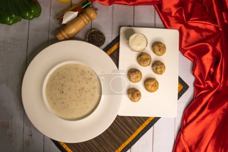 Champignon-Cremesuppe mit schwarzem Pfeffer und Knoblauch-Chilisoße in Schüssel isoliert auf Serviettenoberseite auf Holztisch serviert italienisches Essen
