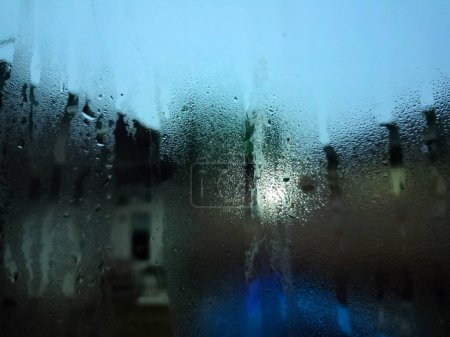 Photo for Rainwater flows down the window pane creating a blurry outside reflection. suitable for backgrounds, presentations and social media. - Royalty Free Image