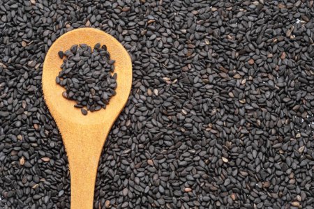 Black cumin seeds in wooden spoon over cumin seeds. Food background.