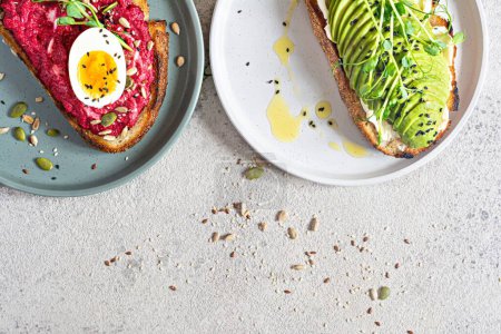 Foto de Whole grain toast with cream cheese, avocado, beetroot hummus, seeds, egg and microgreens (sprouted pea sprouts) on a light gray background. Healthy food concept. - Imagen libre de derechos