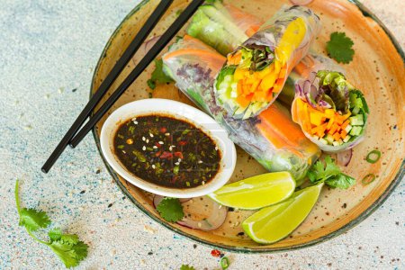 Aperitivo asiático fresco Rollos de primavera (Nem) hechos de papel de arroz y verduras crudas y hierbas con salsa picante sobre un fondo azul claro. Comida vietnamita