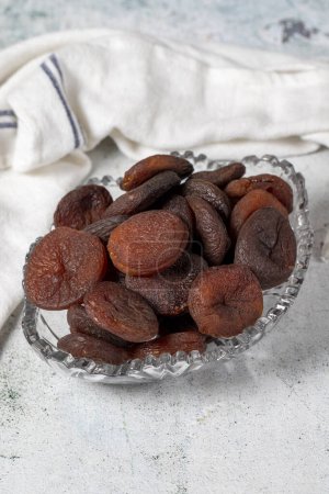 Dried apricots on stone background. Dark dried apricots in a glass bowl. Diet foods. close up