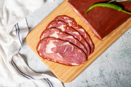 Photo for Beef ribeye pastrami. Dried turkish bacon slice on wooden Cutting Board. Traditional Turkish delicacies. Top view. Local name cemenli pastirma - Royalty Free Image